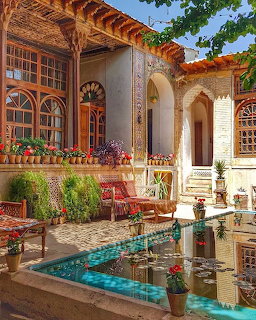Traditional Iranian home courtyard with turquoise pool, arched columns, poted flowers, and colorful cushions