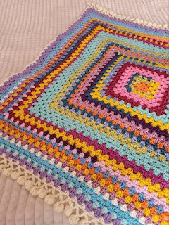Colorful crochet granny square blanket with concentric multicolored rows laid on a white bedspread