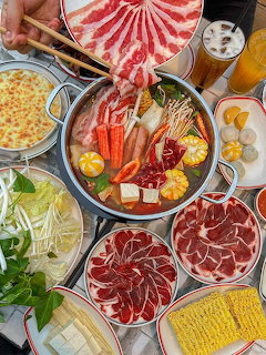 Overhead shot of hot pot meal with beef, seafood, vegetables, and noodles around a central broth pot