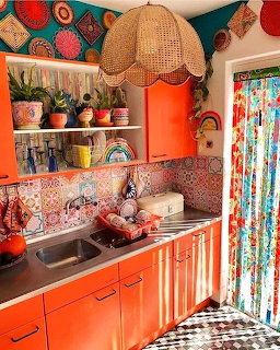 Colorful retro kitchen with orange cabinets, patterned tile backsplash, woven pendant light, and floral curtains