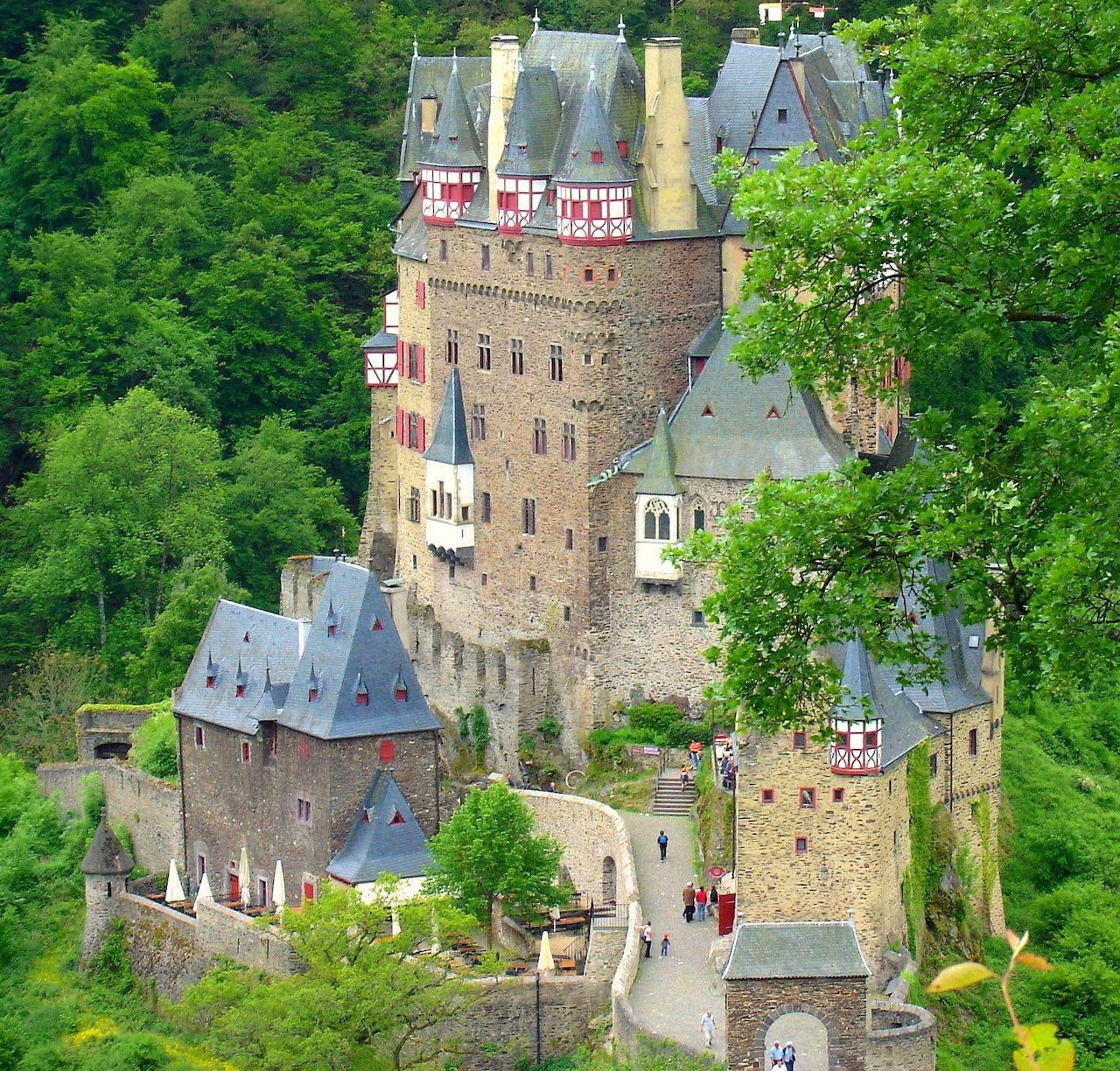 Medieval Eltz Castle surrounded by dense green forest, aerial view showing multiple towers and traditional architecture