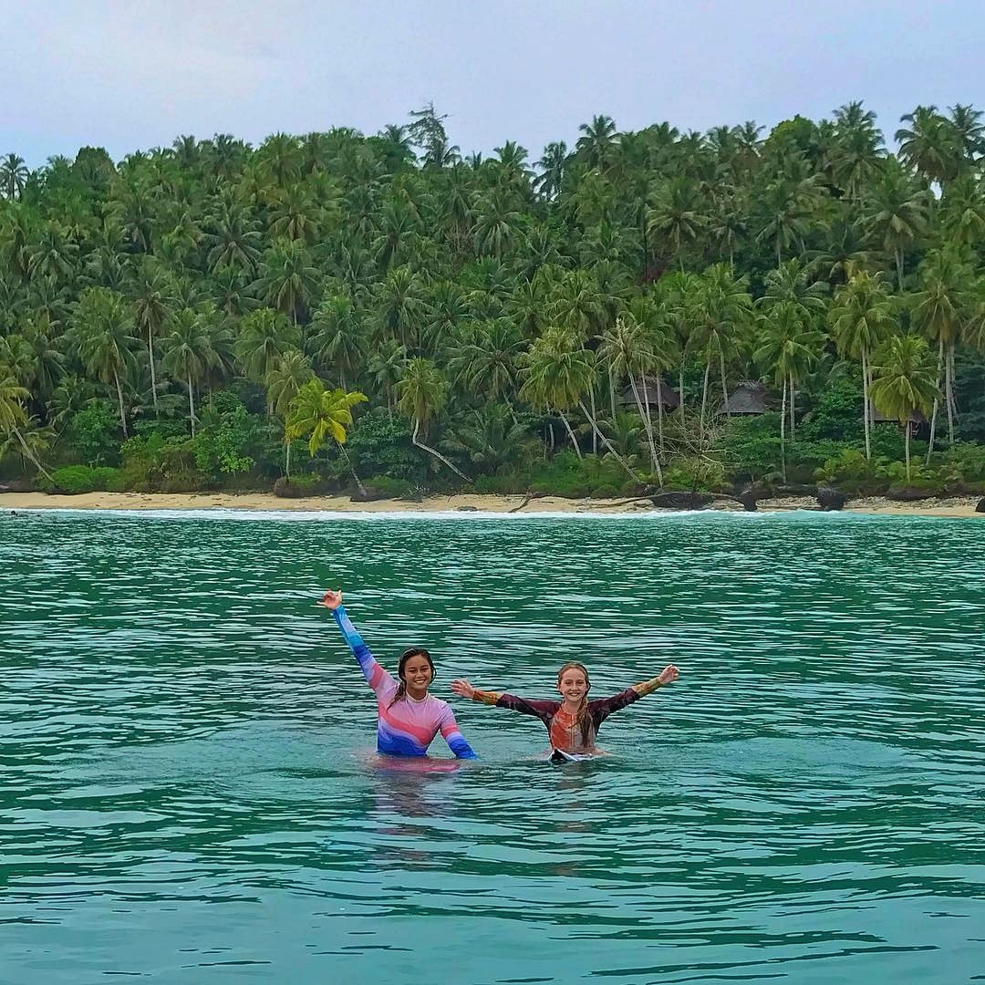 Two surfers in tropical ocean with palm trees on shore