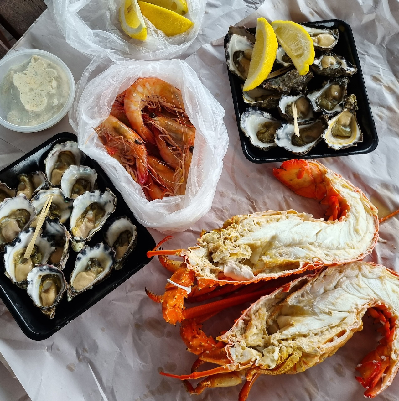 Seafood spread with split lobster, oysters, prawns, lemon wedges, and sauces on a white table