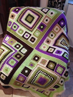 Crocheted patchwork blanket with purple and green granny square patterns draped over a chair