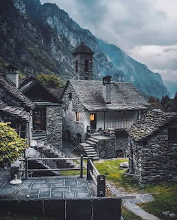 Stone chapel with bell tower in Swiss mountain village beneath towering cliff face