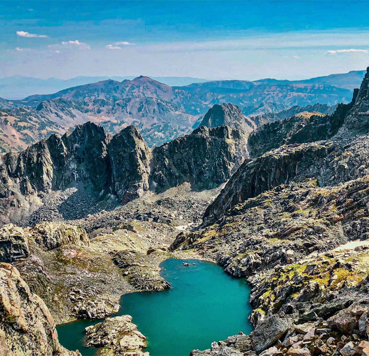 Turquoise lake nestled among rocky mountain peaks with distant mountain ranges under blue sky
