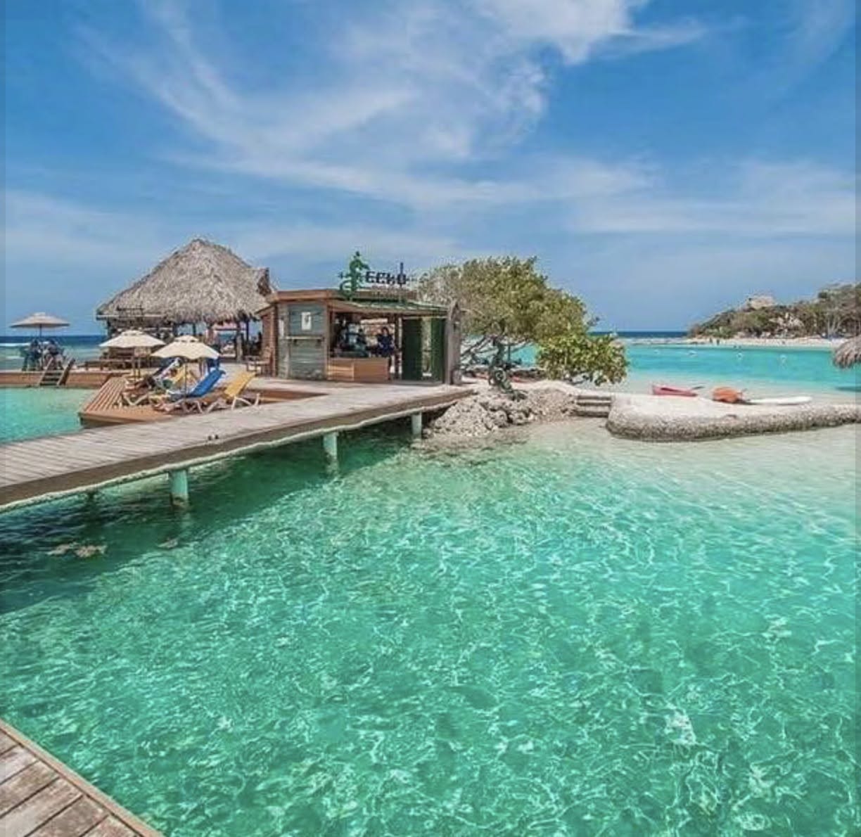 Thatched bungalow on a wooden pier above clear turquoise water with loungers and a small boat