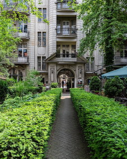 Green courtyard garden with hedges and a path leading to a classical building entrance