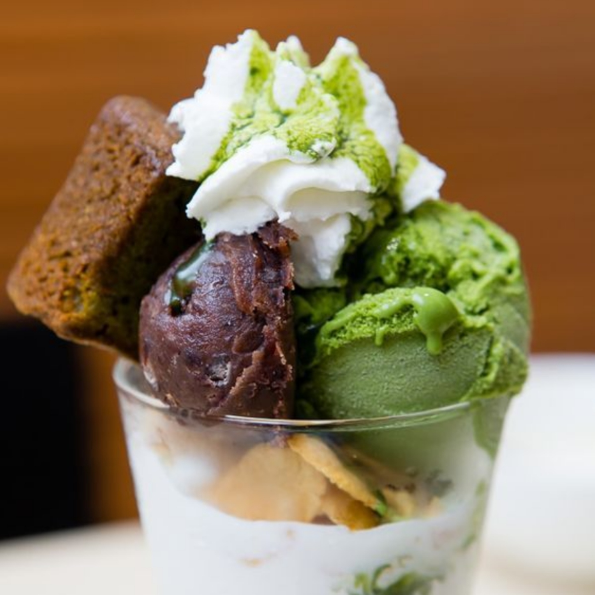 Matcha ice cream parfait with whipped cream, red bean, and cake pieces in a glass