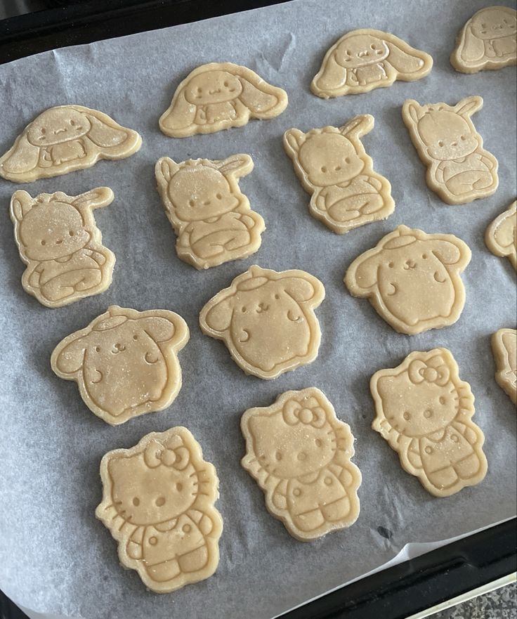 Unbaked Sanrio character cookies including Hello Kitty and Cinnamoroll on baking sheet