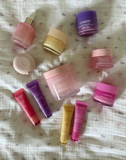 Assorted Laneige skincare products in pink, purple, and yellow arranged on white fabric