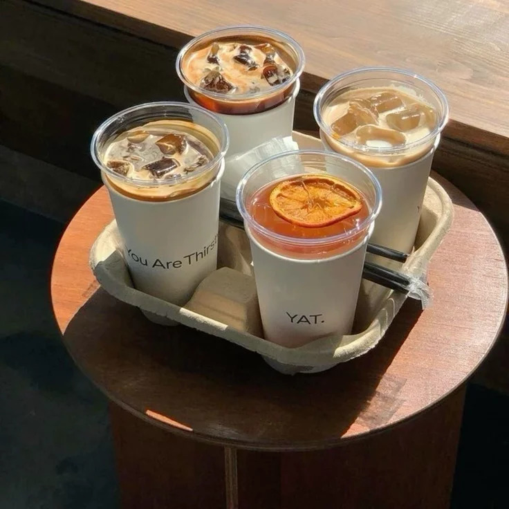 Four iced coffee drinks in takeaway cups on a cardboard tray atop a round wooden table