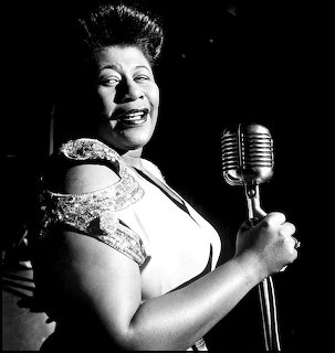 Black-and-white portrait of Ella Fitzgerald smiling beside a vintage microphone