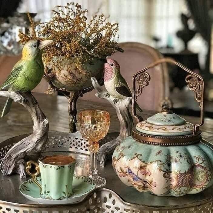 Vintage teapot and teacup with bird figurines on a table indoors