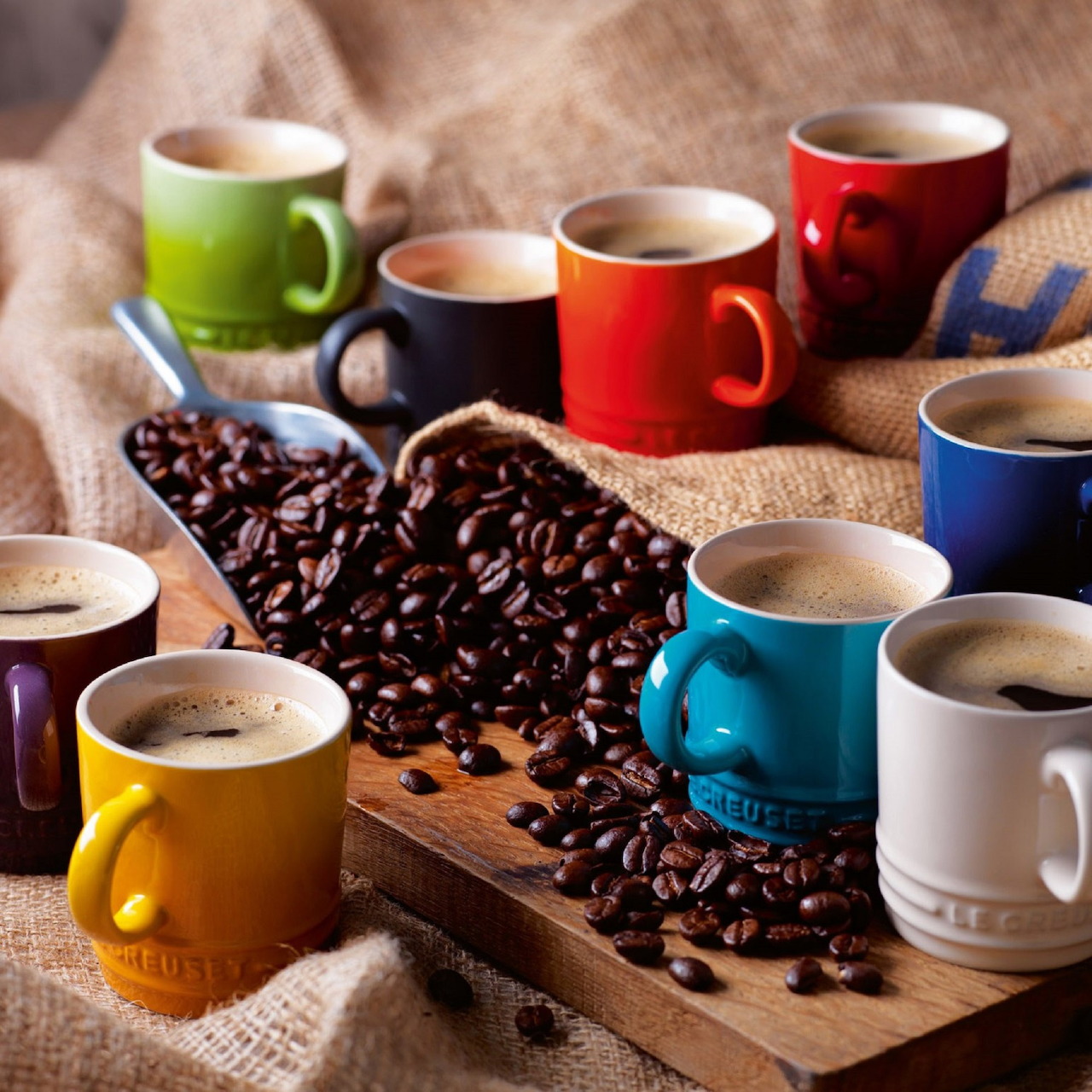 Colorful coffee mugs filled with coffee surrounded by scattered coffee beans on rustic wooden surface