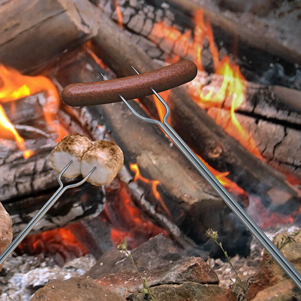 Hot dogs and marshmallows cooking on roasting sticks over a campfire with orange flames