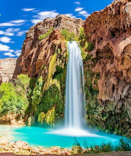Tall waterfall flowing down red rock cliffs into a bright turquoise pool with lush green plants