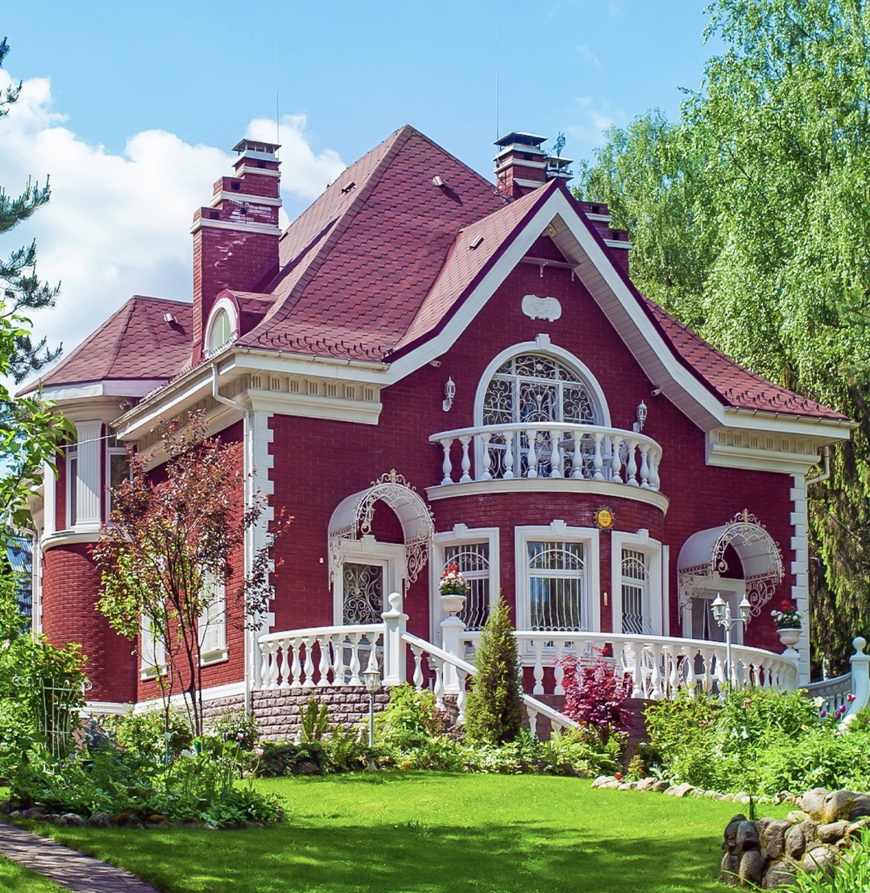 Red brick Victorian house with white trim, arched windows, and a green lawn garden
