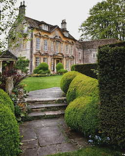 Stone manor house with formal garden featuring rounded topiary hedges and stone pathway steps