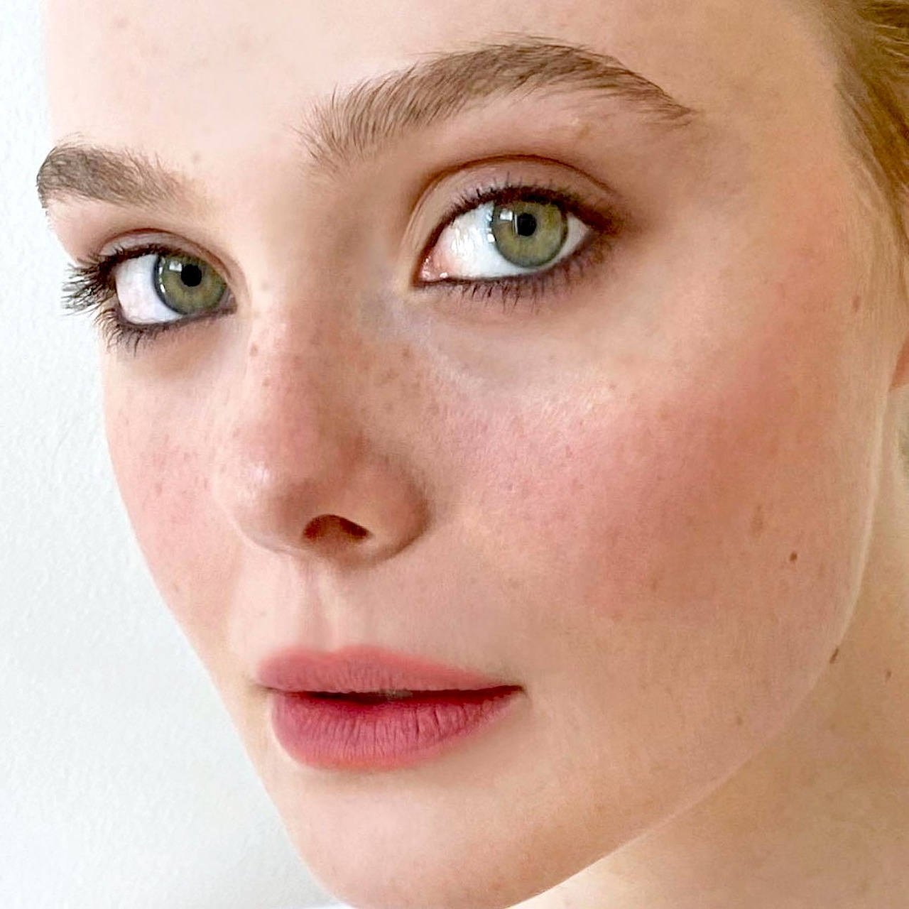 Close-up portrait of a young woman with green eyes and fair skin against a light background