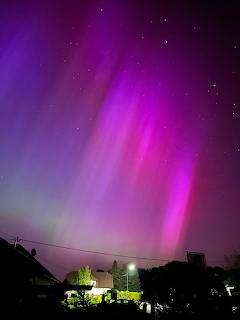Aurora borealis with pink and purple light columns over a dark residential area at night