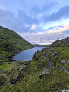 Narrow lake in a rocky green mountain valley beneath a cloudy sky