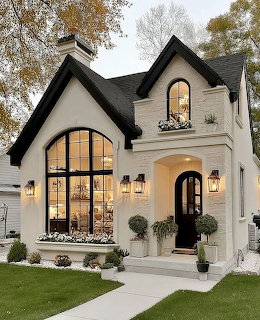 White cottage home with black roof, arched windows, front entry porch, and green lawn