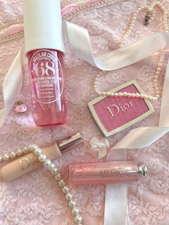 Dior makeup products including lip gloss and blush arranged on pink lace with pearl necklaces