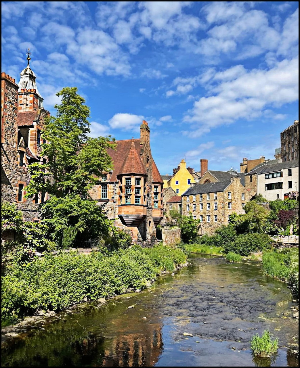 Stone houses and a river in Dean Village, Edinburgh, beneath a blue sky with clouds