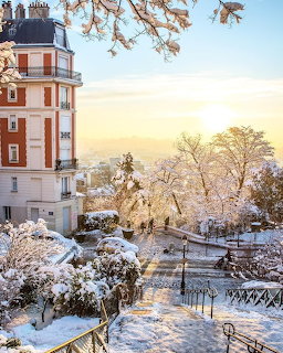 Snow-covered Montmartre street in Paris with golden sunrise light on buildings and trees