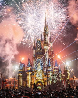 Fireworks exploding above an illuminated castle at night with crowd below