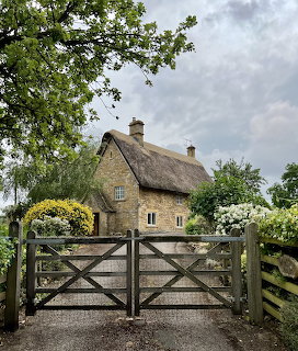 Thatched cottage with stone walls behind wooden gate in English countryside