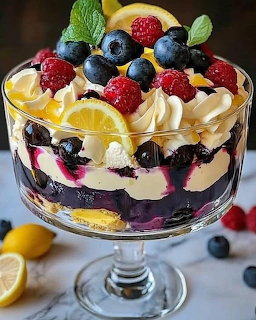 Layered trifle dessert with lemon custard, blueberries, raspberries and mint garnish in glass bowl