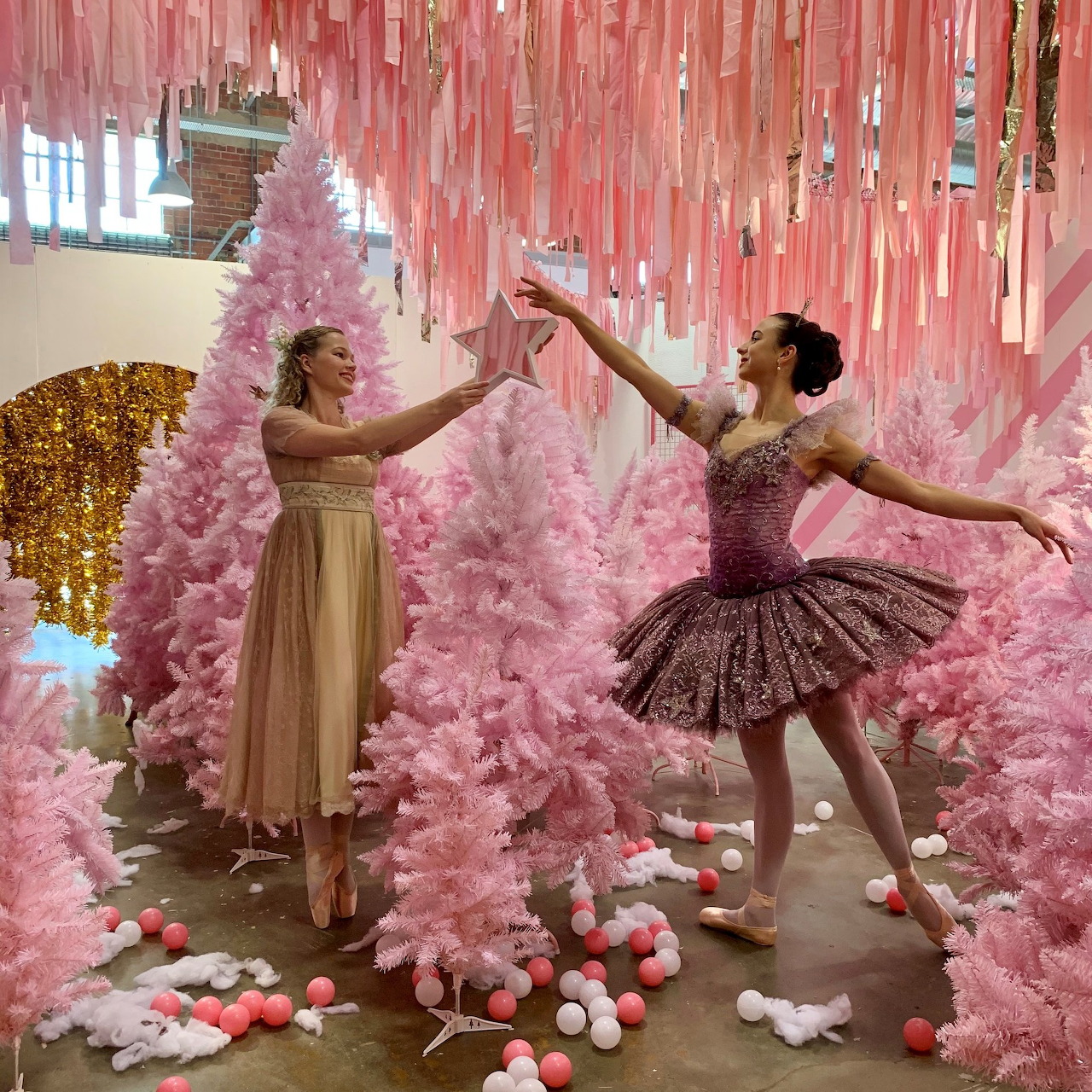 Two ballet dancers in Nutcracker costumes pose gracefully among pink Christmas trees and holiday decorations