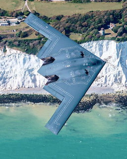 B-2 Spirit stealth bomber flying above white sea cliffs and turquoise water