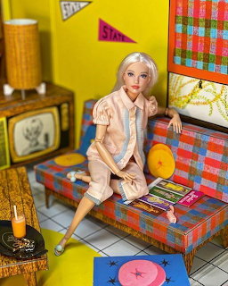 Vintage Barbie doll sitting on a plaid couch in a retro miniature dollhouse living room