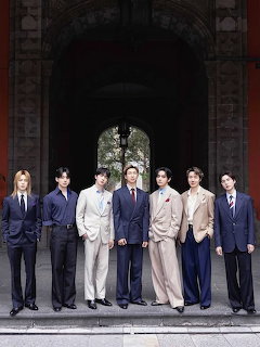 Seven young men in suits standing in a row in front of a large arched stone entrance