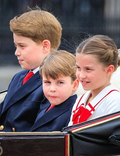 Three children in navy blazers sitting together in a cariage at a formal occasion