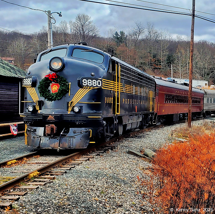 Blue vintage train engine with Christmas wreath on front pulling passenger cars on railroad tracks in winter