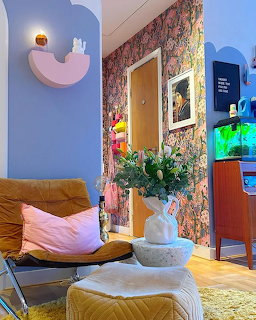 Colorful eclectic living room with leather chair, floral wallpaper, flower vase, and illuminated fish tank