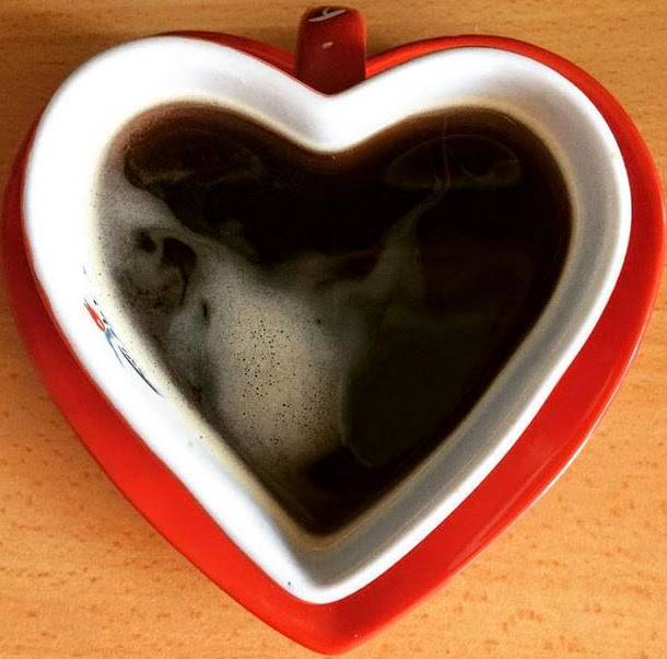 Overhead view of black coffee in a heart-shaped white and red mug on wood table