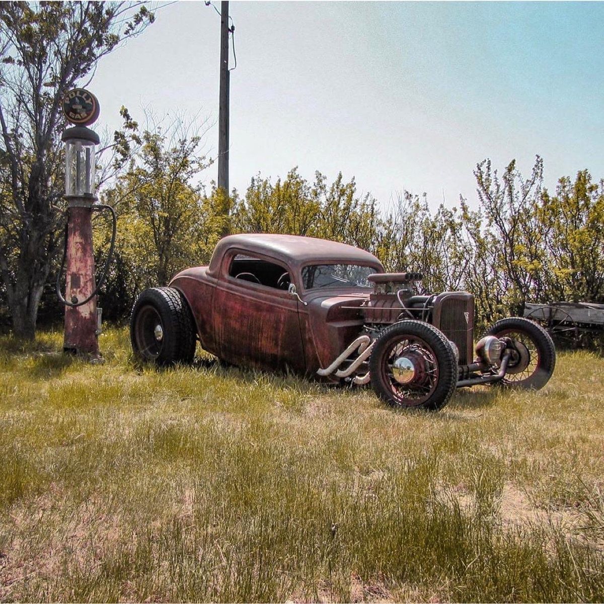 Rusty custom hot rod car with exposed engine in grassy field