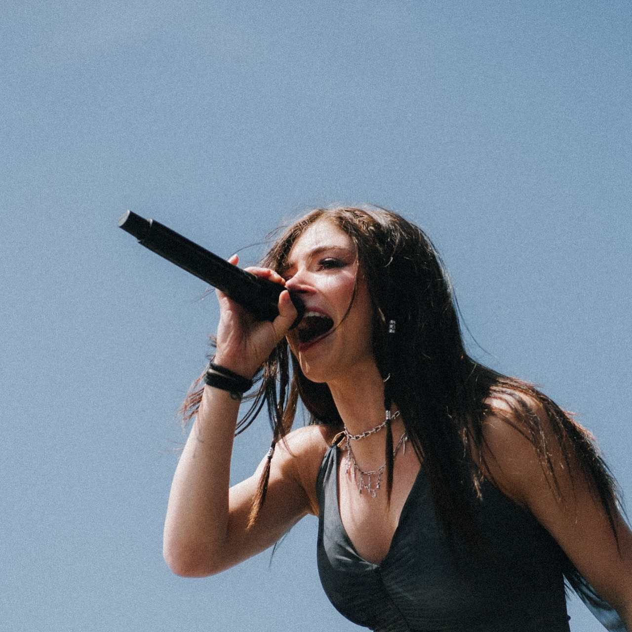 Chrissy Costanza singing into a microphone on stage against a blue sky