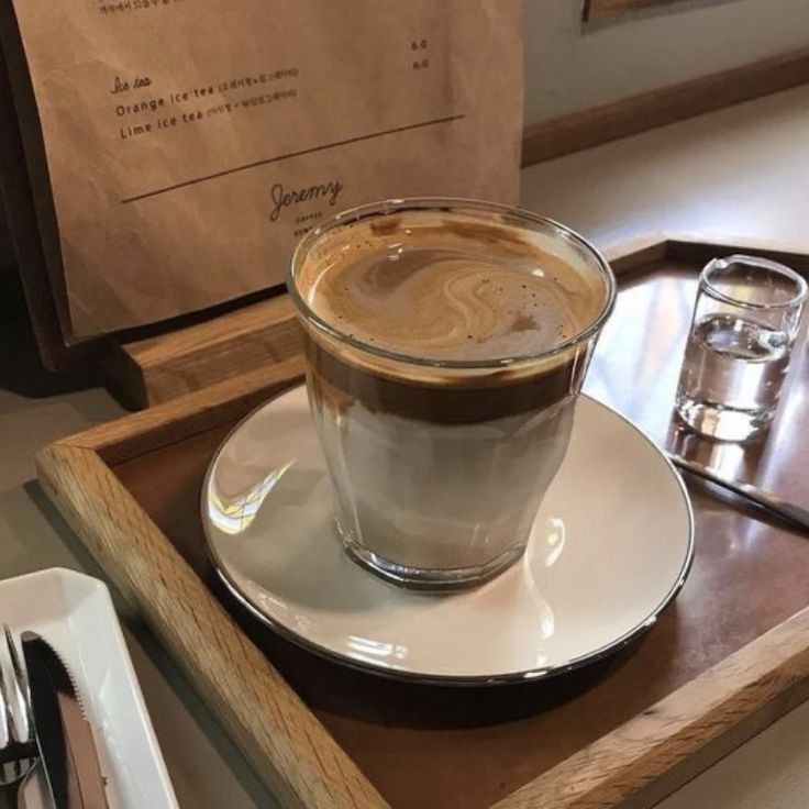 Layered coffee in a glass on a saucer and wooden tray with a small glass of water