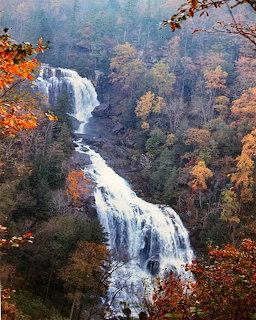 Multi-tiered waterfall cascading through an autumn forest gorge with orange and red foliage