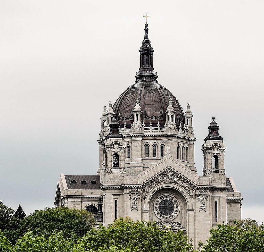 White stone cathedral with large central dome, twin towers, and ornate architectural details under gray cloudy sky