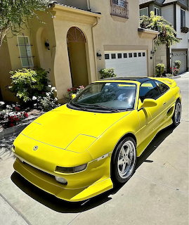 Yellow Toyota MR2 Turbo sports car parked in front of beige stucco house with white garage door