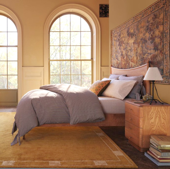 Bright classic bedroom with arched windows, upholstered bed, bedside table, and lamp
