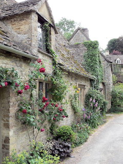 Stone cottage with flowering roses and green ivy climbing weathered walls along a village path