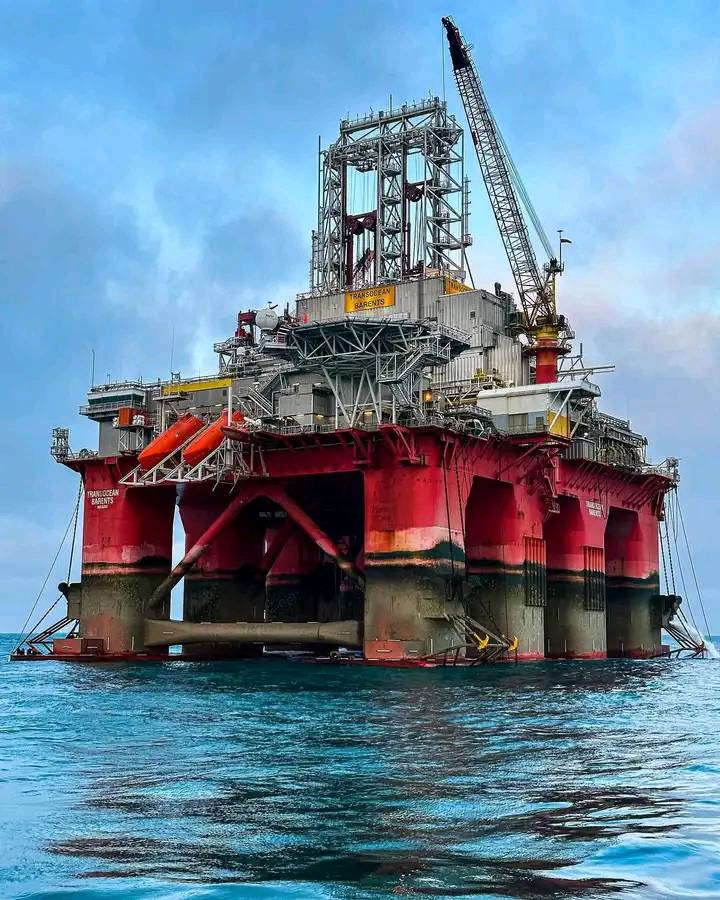 Red and grey offshore oil rig platform in the ocean with crane and overcast sky